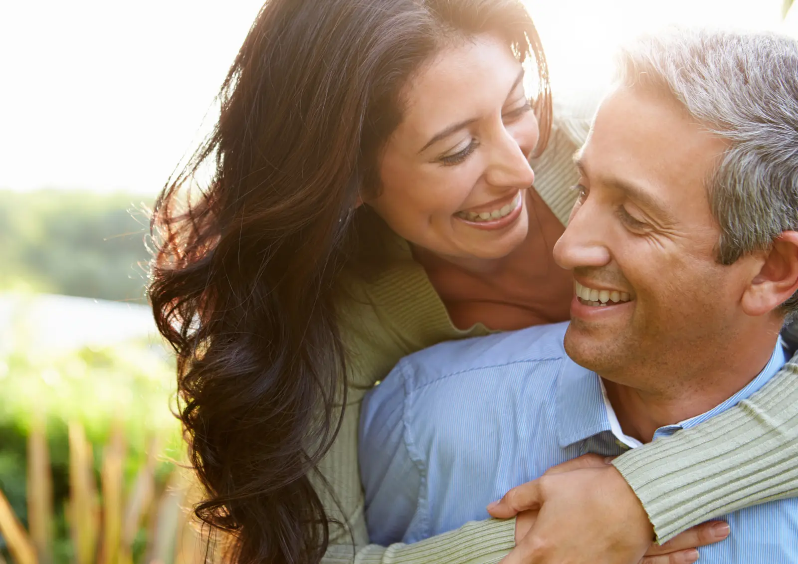 Casal sorrindo, abraçados ao ar livre